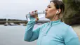 A woman drinking from a clear water bottle during an outdoor workout.
