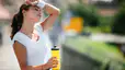A tired athlete rubbing sweat off her forehead with her sweatband and drinking from a yellow water bottle. Learn how to rehydrate in this article.