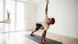 A man doing yoga before or after a workout. He's doing Triangle Pose on a yoga mat at home.