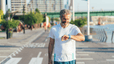 A man looking at his sports watch while walking outside for five minutes.
