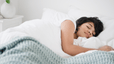 A woman sleeping peacefully in a bright, sunny bedroom. Learn how many hours of REM sleep you need in this article.