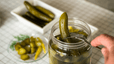 A close-up photo of someone using a fork to take a pickle out of a pickle jar.