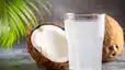 A clear glass of coconut water sitting in front of coconuts. There are many health benefits of coconut water.