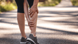 A close-up photo of a woman grabbing her cramping calf muscle during an outdoor run.