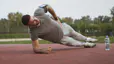 Man in gray t-shirt and sweatpants doing a side plank outside 
