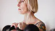 Woman with tattoos holding two kettlebells racked at shoulder height while doing kettlebell shoulder exercises
