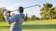 Man swinging golf club on course