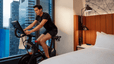 A man riding a Peloton Bike in his Hilton brand hotel room.
