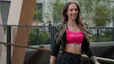 Peloton instructor Kirra Michel going on a walking meditation outdoors. She's smiling and wearing a pink Peloton sports bra, a black zip-up hoodie, and black jeans.