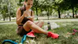 A woman eating a meal from a container while sitting in the grass outside. She's wearing workout clothes.