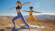 Two women in Peloton apparel doing yoga outside in a desert reaping the mind and body benefits of yoga.