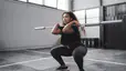 Woman does a squat with a barbell bar without weights, a beginner barbell exercise