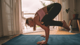Woman practicing Crow Pose on a mat while doing yoga at home.