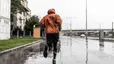 Man running in the rain through a city in an orange rain jacket