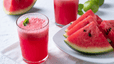A glass of watermelon juice garnished with fresh mint leaves sitting next to a plate of other watermelon slices.