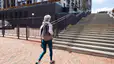 Woman wearing a backpack walks towards steps outside