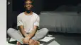 A man calmly sitting on the floor and meditating in his bedroom. Check out eight meditation tips in this article.