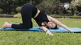 A young woman doing yoga outside on grass does the thread the needle stretch