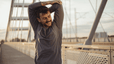 A man smiling and stretching his arms before going on an outdoor run in the morning.