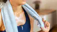 A close-up photo of a sweaty woman cooling down after a workout. She's holding a towel around her neck.