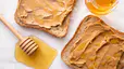 A honey stick sitting near two slices of peanut butter toast that also have honey on them.