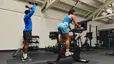 Two friends doing strength and cardio workouts side by side in a gym using a Peloton Bike.