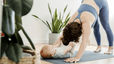 A woman practices down dog yoga pose with a baby near her 
