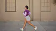 Woman in a purple shirt and grey shorts doing the run-walk method outside past a blank wall