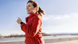 A happy woman going a run outside. She's wearing a red zip-up hoodie.