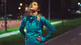 An exasperated athlete on an outdoor running path in the evening, with her hands on her hips and head pointing up to the sky. She has lost motivation to work out.