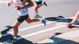 A close-up photo of runners' lower bodies quickly running a marathon.