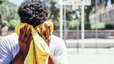 A man wiping away sweat from his face with a clean towel after an outdoor basketball game to prevent sweat pimples.