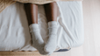 A close-up photo of a woman sleeping with socks. Her socks are gray and her feet are popping out from under the covers on her bed.