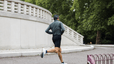 A photo of a man from the back as he goes on a run outdoors. He's wearing biker shorts, a long sleeve shirt, and sunglasses.