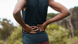 A close-up photo of a runner with their hands on their lower back, experiencing pain.