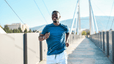 A smiling man running across a bridge on a sunny day.