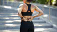 An athlete holding her lower back while standing outside in athletic clothes. She is experiencing lower back pain after squats.