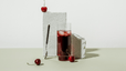 A glass of tart cherry juice propped against a cinder block with tart cherries and a spoon nearby.