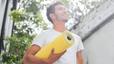 A man holding a yellow yoga mat and smiling while standing outside. Learn how to motivate yourself to work out here.