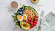 A wholesome bowl filled with macronutrient sources, including avocado, hard-boiled egg, chickpeas, spinach, tomato, blueberries, and cucumbers.