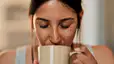 Does Coffee Dehydrate You?: Close-up photo of a woman with freckles drinking a cup of coffee from a mug.