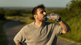 A man drinking water during a workout. He's outside on a sunny day.