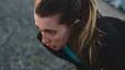 A young woman with a ponytail is bent over outside with her hands on her knees, experiencing nausea after a workout.