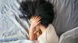 A woman lying in bed on her side as she has morning anxiety. Her hand is covering her face.