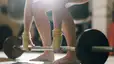 A zoomed-in photo of a woman working out barefoot. She's about to perform a deadlift with a barbell.