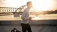 Side view of a man jogging outside near a river in the morning sunlight.
