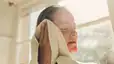 A woman drying her face with a towel as she's sweating after a shower.