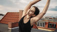 A woman doing yoga on a rooftop to ease anxiety. She's stretching to one side with her arms over her head and her eyes closed.