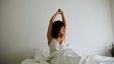 A woman stretching her arms above her head in bed after waking up.