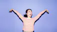 A woman smiling and spreading out her arms energetically. She's wearing a red and white striped shirt and standing against a lavender background. Learn how to get more energy in this article.